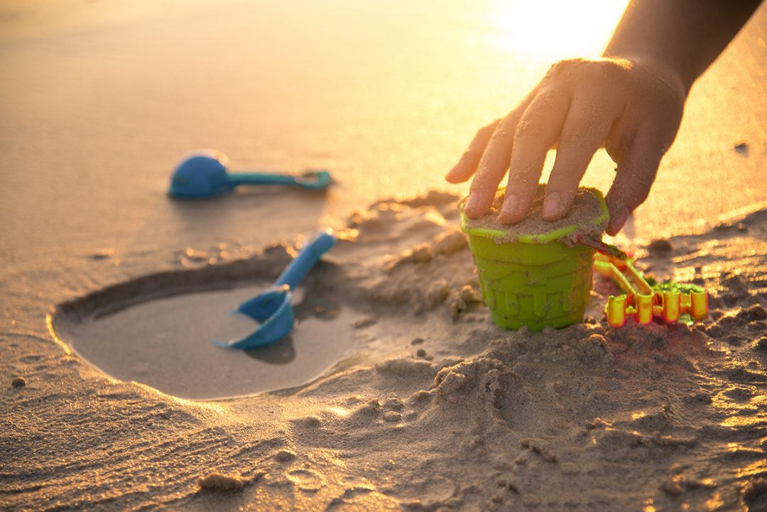Barn bygger med sand i solnedgang